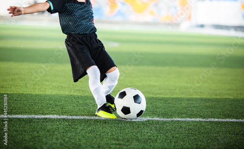 Selective focus to football with motion blur of kid soccer player shoot it on artificial turf. Soccer player training for football match.
