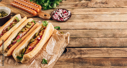 Barbecue grilled hot dog with pickled cucumber, red onion and mustard on rustic wooden background. Selective focus