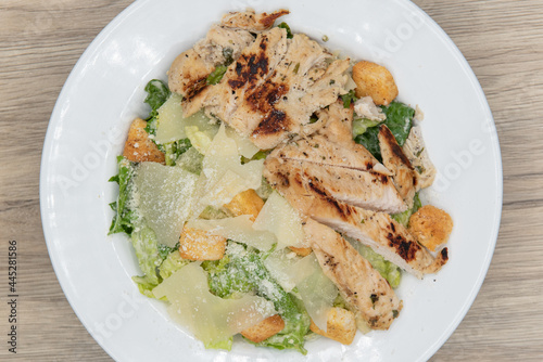 Overhead view of large grilled chicken breast cut up and topping this very hearty caesar salad in a bowl