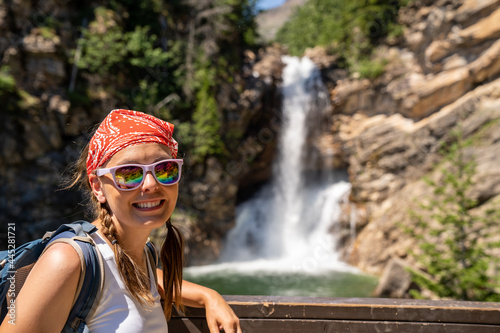 Fototapeta Naklejka Na Ścianę i Meble -  Cute woman hiker with braided hair wearing a tank top poses at Running Eagle Falls waterfall in Glacier National Park