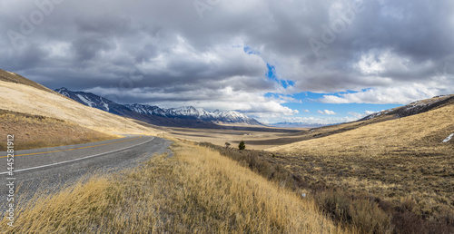 A road curving to the left and revealing an epic mountain and prairie landscape with snow covered peaks in Idaho.