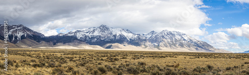 A panorama of distant snow covered mountain peaks with white clouds and blue skies in Idaho.