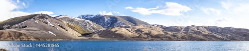 A panorama of snow covered mountains with a lake and blue skies with some white clouds in Idaho.
