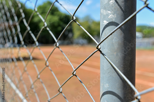 Close-up grids of a tennis court and a blurred sunny day in the background.