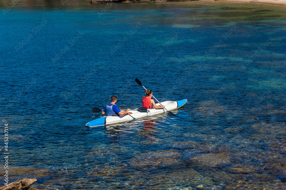 young couple paddling a kayak in crystal clear waters in the sea of buzios.