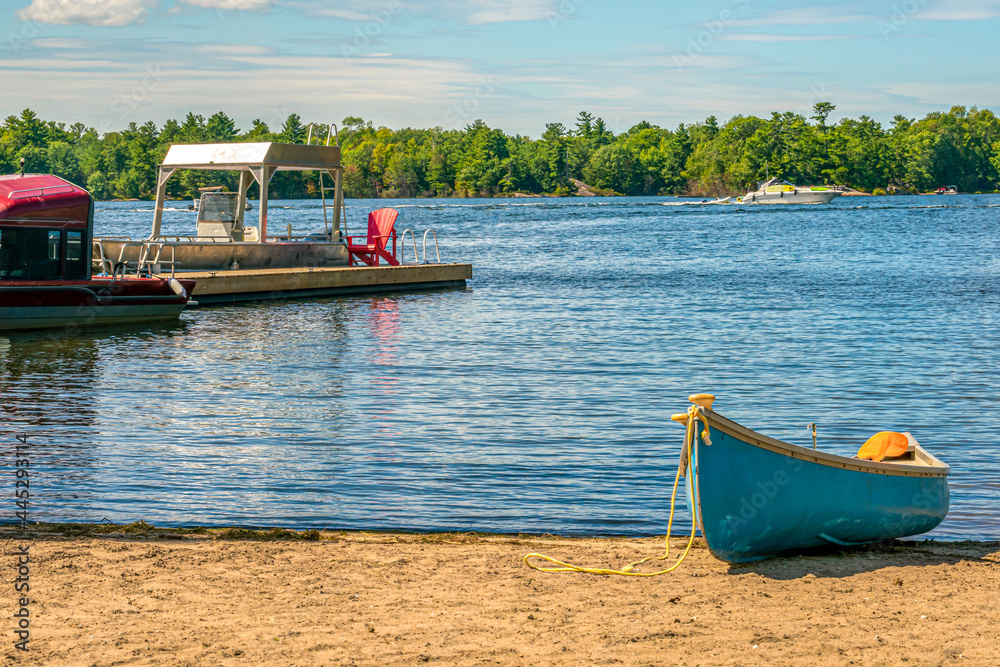 Fototapeta premium Reflections of a summer holiday on a lake with canoe, pontoon boat, fishing boat and speed boats and sandy beach in the foreground. Concept - background, copy space