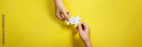 Two hand joining two matching puzzle pieces together in a conceptual image of teamwork and cooperation.