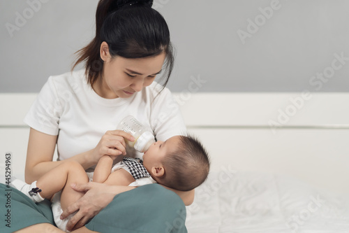 mother feeding milk from bottle and baby sleeping on bed