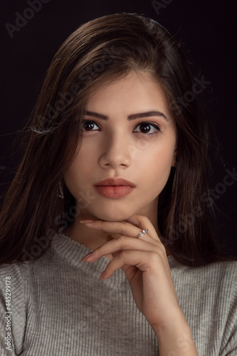 Fashion photo of a beautiful model with long hair  wearing grey top   fashion pose  studio portrait  dark background  close up pic.
