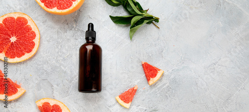 Bottle of essential aroma oil with grapefruit and leaves on light gray background.