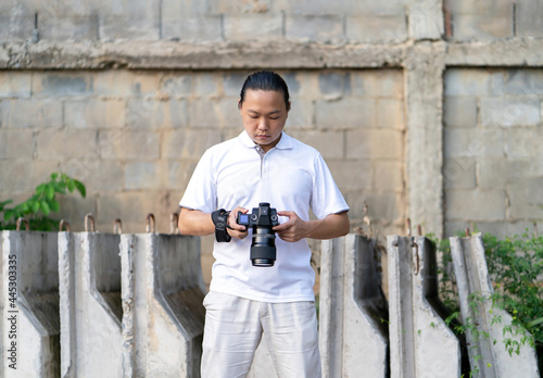 Asian Thai - Chinese professional camera man posts and check image shot via liveview behind Medium format Mirrorless camera with construction background. photo