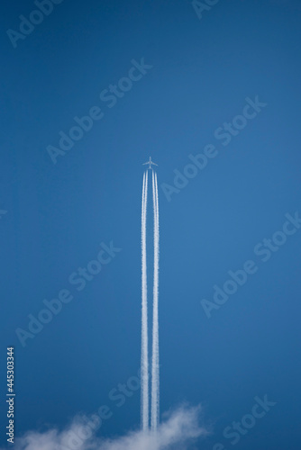 Jet airplane is flying up like a rocket. Long white trails in the blue sky. Vertical photo