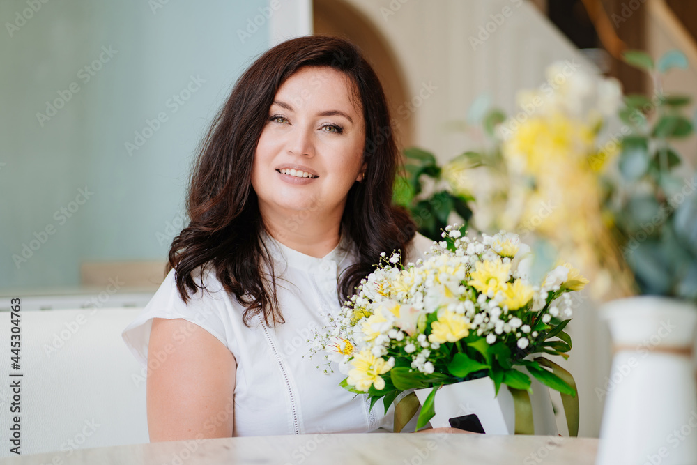 attractive woman in white clothes with flowers at the table in a light room. attractive woman in white clothes with flowers at the table in a light room.