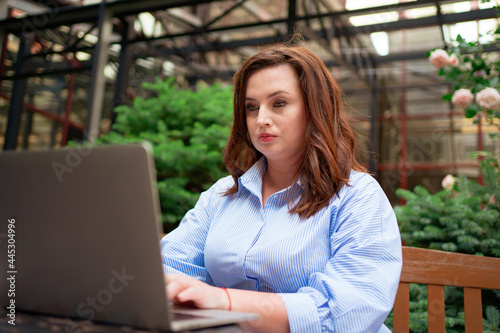 serious woman sits with laptop in cafe on street, communicates with friend