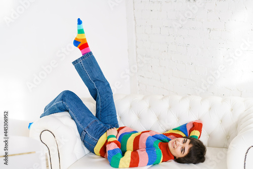 Beautiful girl in rainbow sweater lies on white sofa and smiles. A pretty young woman of Caucasian nationality is looking into the camera. photo