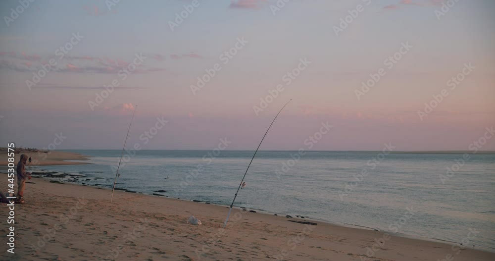 Fisherman With Two Fishing Rods On The Arcachon Bay, Southwest Coast Of France During Sunset - wide shot Fisherman With Two Fishing Rods On The Arcachon Bay, Southwest Coast Of France During Sunset - wide shot