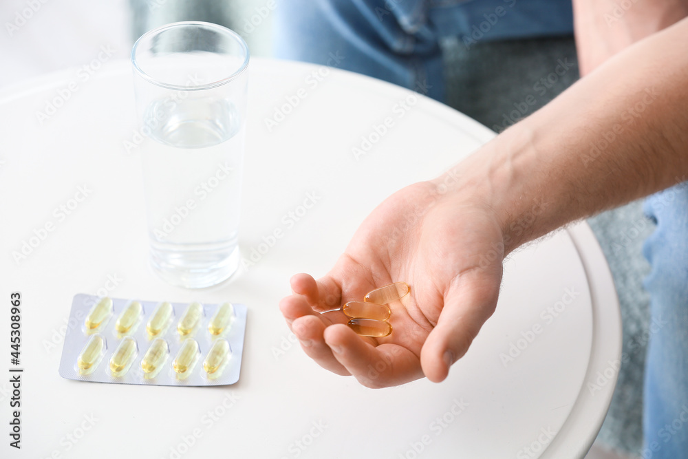 Young man with fish oil pills at home, closeup Young man with fish oil pills at home, closeup