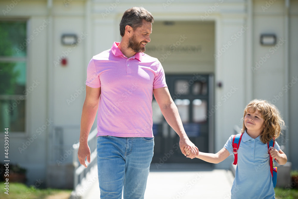 Obraz premium Parent and pupil of primary school go hand in hand. Teacher in t-shirt and cute schoolboy with backpack near school park.