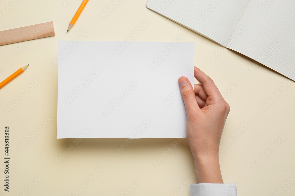 Female hand with blank sheet of paper and stationery on color background Female hand with blank sheet of paper and stationery on color background