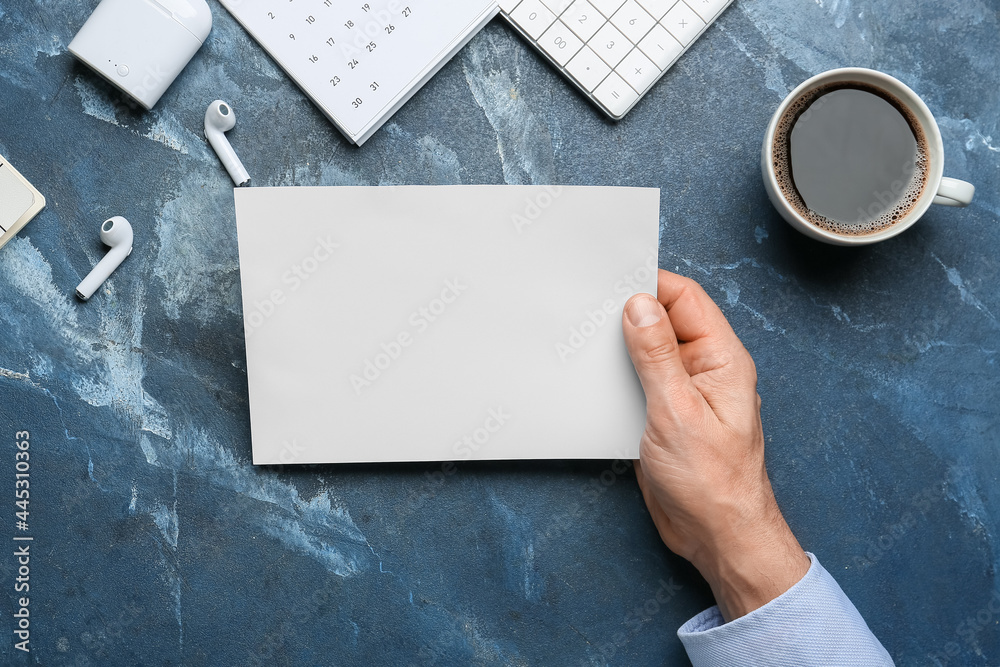 Obraz premium Male hand with blank sheet of paper, earphones and cup of coffee on color background, closeup