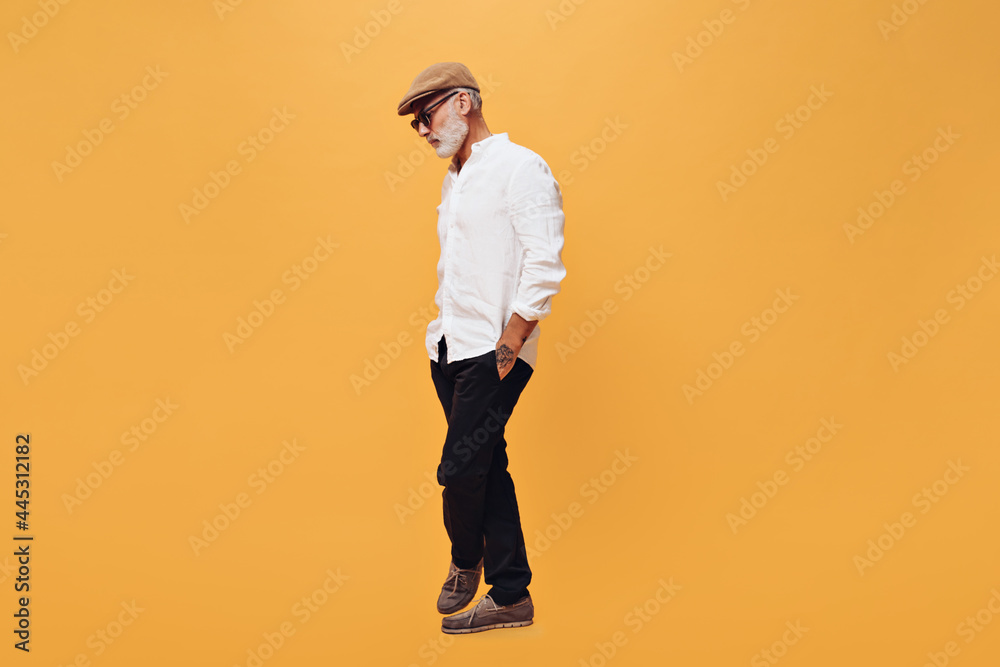 Fototapeta premium Full length portrait of man in white shirt and black pants on orange background. Photo of bearded gray-haired adult guy in fashionable clothes