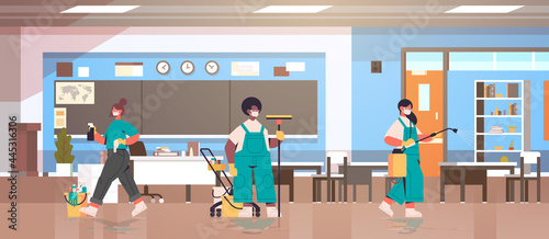 mix race cleaners in masks disinfecting coronavirus cells in school classroom to prevent covid-19 pandemic