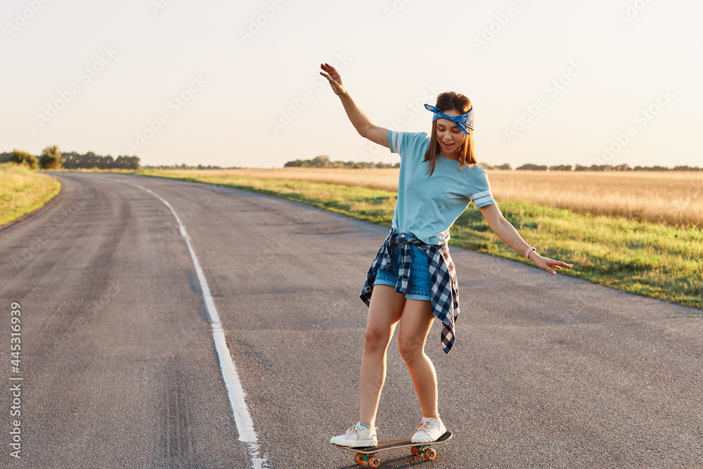 Sporty woman riding on the skateboard on the road., Slim sporty female enjoying longboarding, raising hands , having happy concentrated expression, healthy lifestyle, copy space.