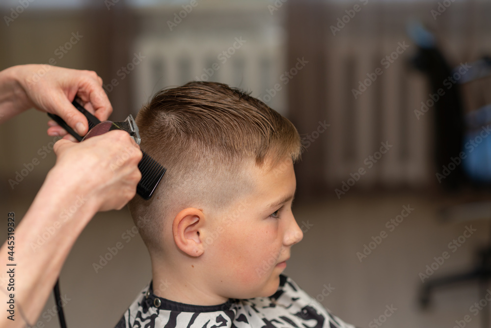 Fototapeta premium Cute kid boy have hair cut, professional barber doing haircut. Hairdress for children. side view portrait barbershop.
