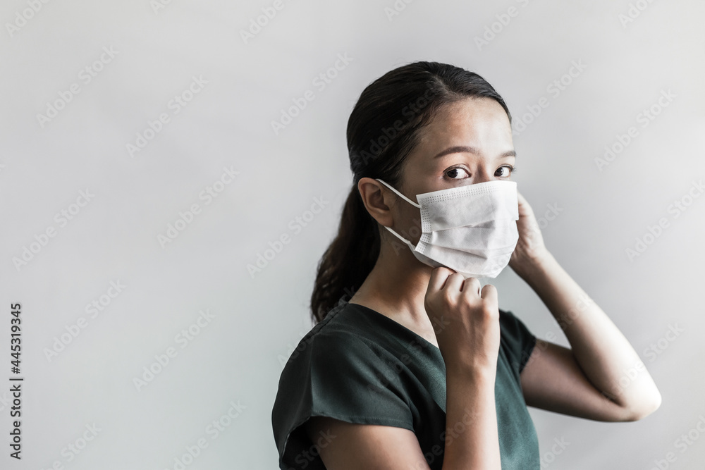 Asian woman wearing protection face mask against coronavirus. Studio shot masked woman looking at the camera and putting mask on her face on grey background. Coronavirus or Covid-19 concept. Asian woman wearing protection face mask against coronavirus. Studio shot masked woman looking at the camera and putting mask on her face on grey background. Coronavirus or Covid-19 concept.
