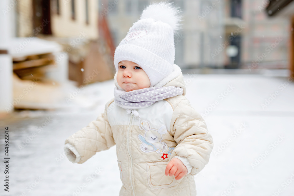 Obraz premium Happy little baby girl making first steps outdoors in winter through snow. Cute toddler learning walking. Child having fun on cold snowy day. Baby's first snow, activity. Winter walk outdoors