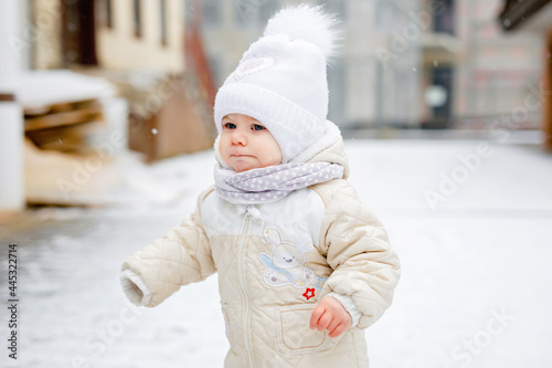 Happy little baby girl making first steps outdoors in winter through snow. Cute toddler learning walking. Child having fun on cold snowy day. Baby's first snow, activity. Winter walk outdoors photo