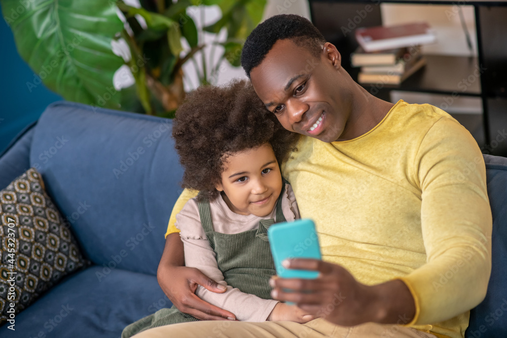 Little girl with dad hugging looking into smartphone Little girl with dad hugging looking into smartphone