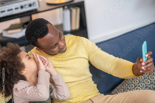 Dad with smartphone in outstretched hand and little daughter