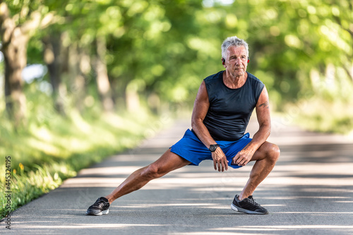 Grey-haired old man still in shape streches legs in his pre-workout warmup photo