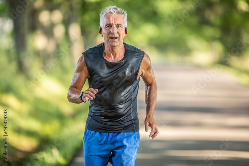 Muscular older man in good shape runs outdoors and sweats during a run with his earphones on