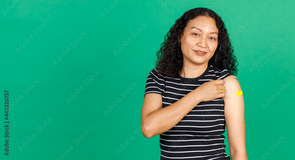 Asian middle aged woman holding her arm with bandage patch showing she got vaccinated for Covid 19 virus on green background. Concept for Covid 19 vaccination Asian middle aged woman holding her arm with bandage patch showing she got vaccinated for Covid 19 virus on green background. Concept for Covid 19 vaccination