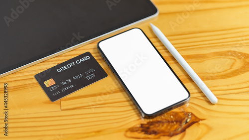 Online payments concept, Smartphone blank screen for advertisement with credit card, tablet and stylus pen on wooden table