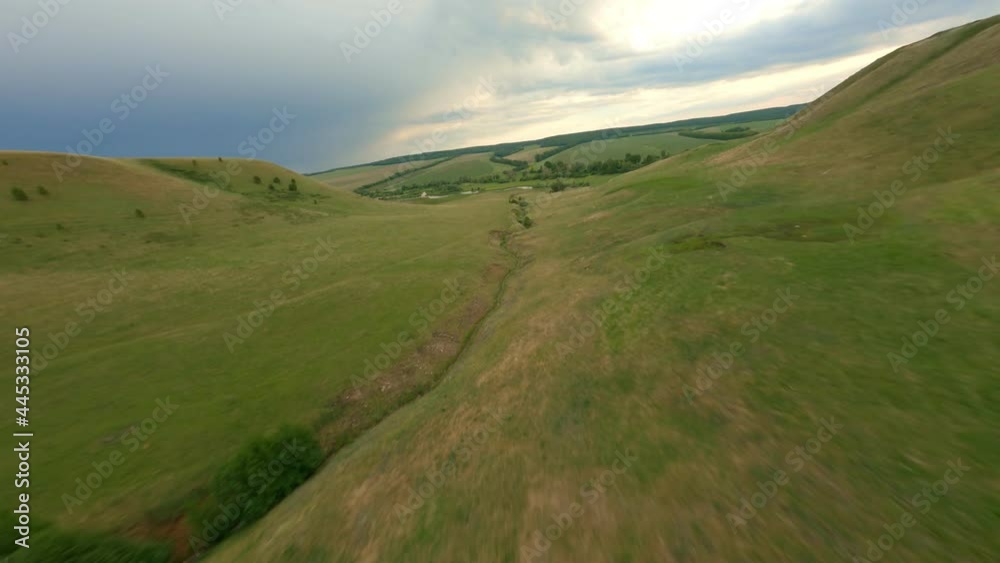 Green hills in the valley descend to the river. Wildlife. A small ravine overgrown with dense vegetation. Evening in the valley, the sky with dark rain clouds. High quality. 4k footage.