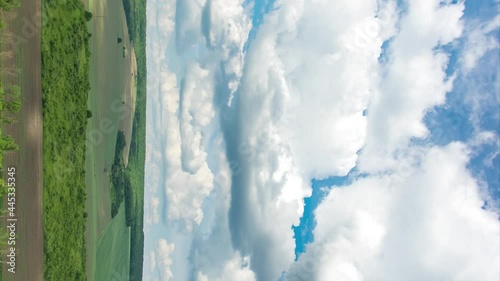 Timelapse of clouds over a field and forest on a summer day, vertical video