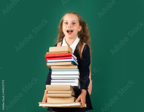 Knowledge day, Smiling funny little schoolkid girl with backpack hold books on green blackboard. Childhood lifestyle concept. Education in school.