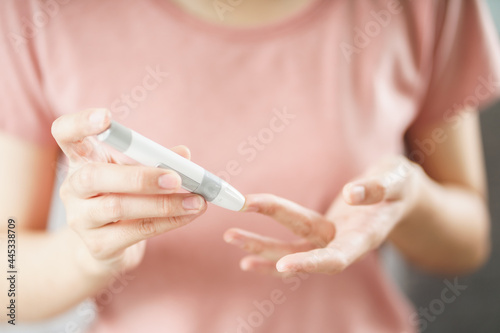 Asian woman using lancet on finger for checking blood sugar level by Glucose meter, Healthcare and Medical, diabetes, glycemia concept