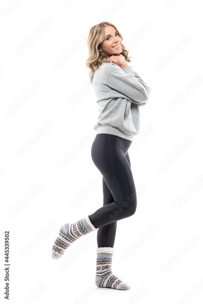 Fototapeta premium Side view of happy young woman in gray hooded sweatshirt posing with raised leg. Full body isolated on white background.