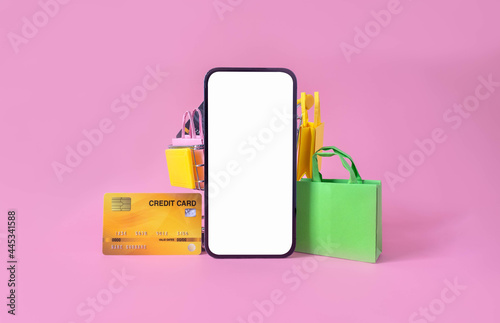 Shopping and payment with smartphone white screen and shopping bag, credit card in cart on pink background.Consumers can buy everything from online stores using a smart device connects to internet.