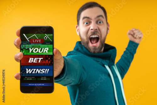 Man being happy winning bet in online sport gambling application on mobile phone, screaming and clencing his his fist photo
