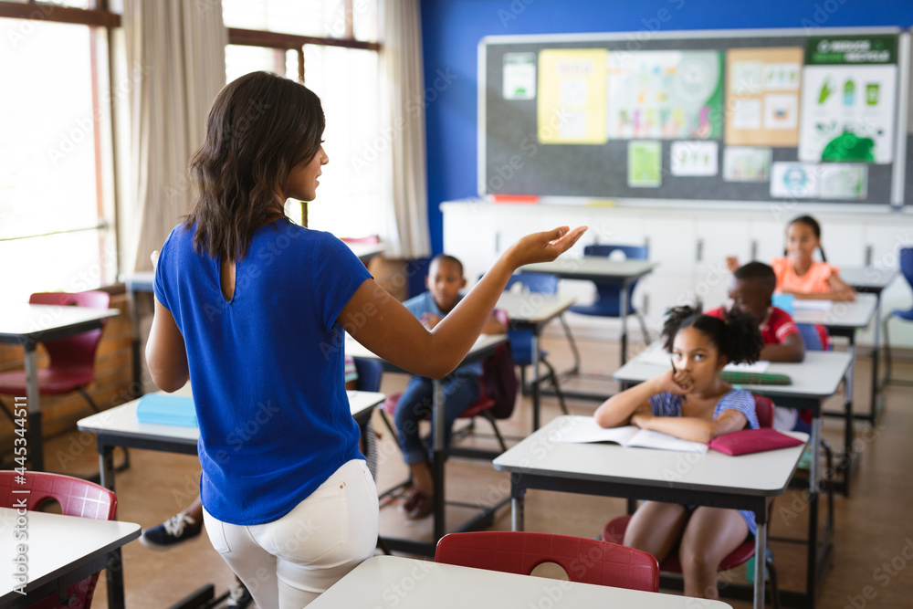 Rear view of african american female teacher teaching students in the class at elementary school Rear view of african american female teacher teaching students in the class at elementary school