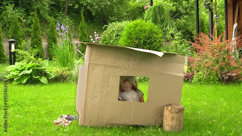 Girls play in a cardboard house near the house on the lawn. High quality 4k footage