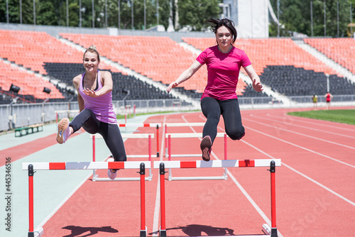 Two female sportswomen are jumping over an obstacle. Running with hurdles. Active lifestyle