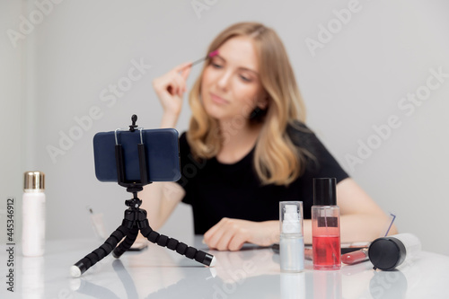 Beauty blogger young woman records video tutorial of course on facial skin and eyebrow care on phone