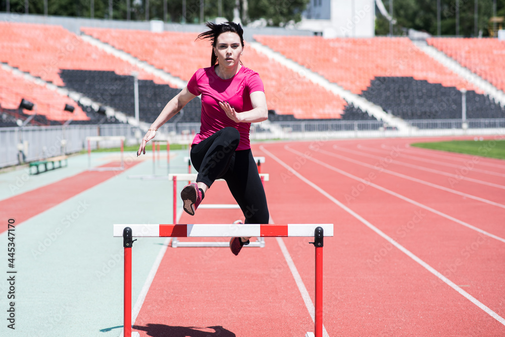 Obraz premium Woman athlete jumping over an obstacle. Running with hurdles. Active lifestyle