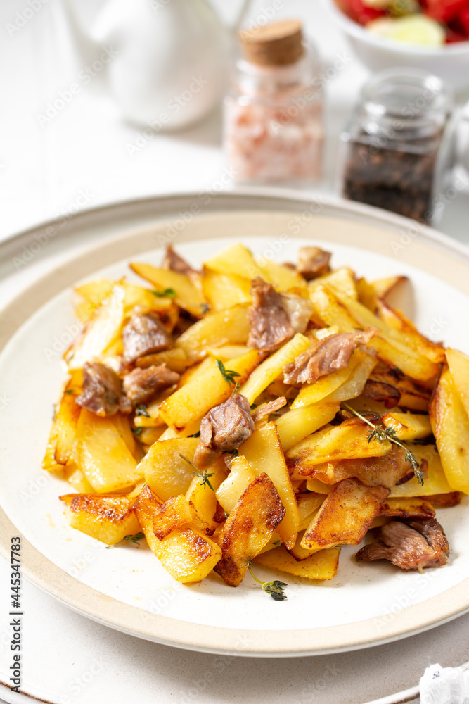 Fried potatoes with turkey meat and thyme in a plate on a white culinary background closeup Fried potatoes with turkey meat and thyme in a plate on a white culinary background closeup